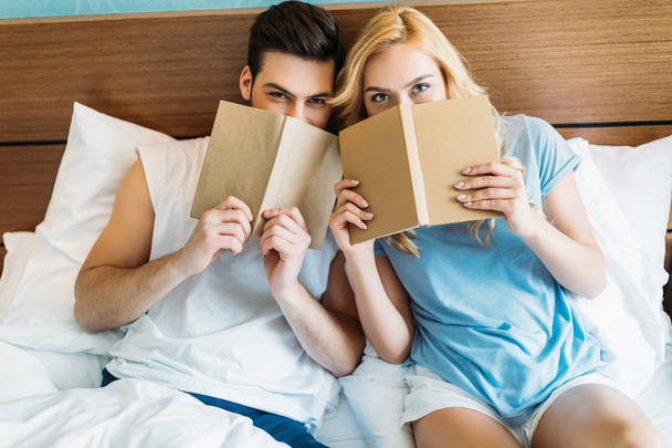 smiling couple looking out from books in bed - Foto, Bild
