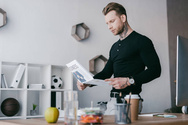 handsome young tattooed businessman reading newspaper in office - Valokuva, kuva