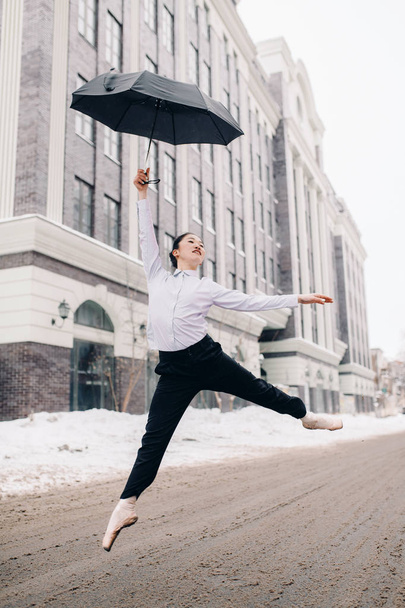 Ballerina met paraplu in haar handen is hoog springen op stad straat. - Foto, afbeelding