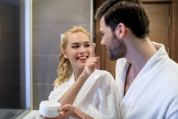 smiling girlfriend applying cream on boyfriend face - Foto, imagen