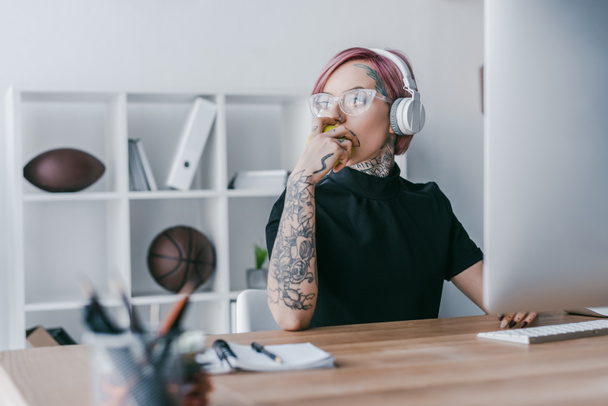 fiatal tetovált üzletasszony fejhallgató keres el a munkahelyen  - Fotó, kép