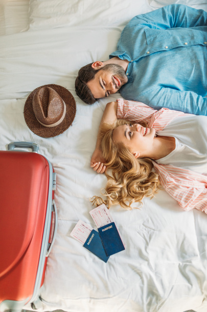 overhead view of couple of tourists lying on bed in hotel room - Photo, Image