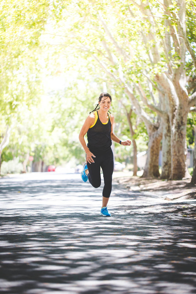 Beautiful brunette female fitness model running outside in a leafy and green suburb - Photo, Image