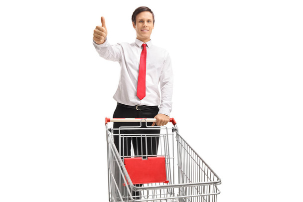 Formally dressed man with an empty shopping cart making a thumb up gesture isolated on white background - Photo, Image