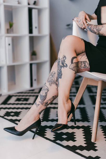 Schnappschuss einer jungen Geschäftsfrau mit Tätowierungen, die auf Stuhl im Büro sitzt - Foto, Bild