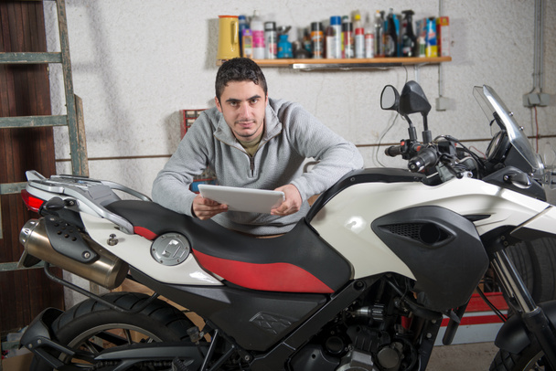 a young man using a tablet next to motorcycle - Photo, Image