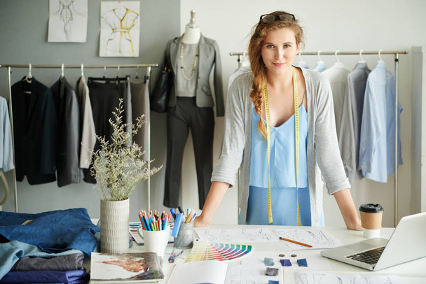 Портрет веселой владелицы модной студии, стоящей за рабочим столом
 - Фото, изображение