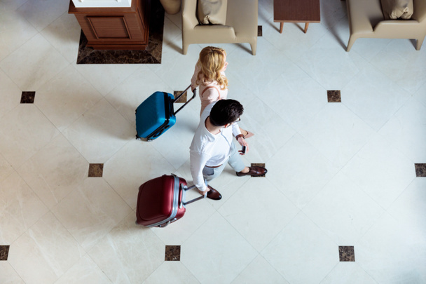 overhead view of couple of travelers walking with luggage in hotel - Photo, Image