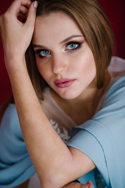 Mooie jonge vrouw met make-up in blauwe jurk poseren in studio - Foto, afbeelding