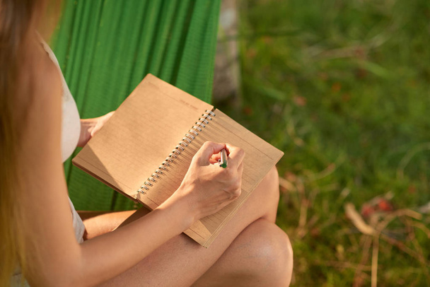 γυναίκα λήψη σημειώσεων ενώ οι δαπάνες καλοκαιρινή μέρα, μέσα σε καταπράσινο κήπο - Φωτογραφία, εικόνα