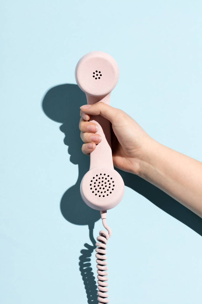 Woman's hand holding a pastel telephone on a blue background. Telecommunication. - Foto, immagini