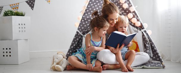 Familienmutter liest Kindern im Zelt zu Hause vor - Foto, Bild