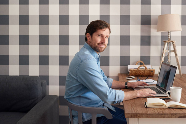 Confident business owner working online with laptop at table in his living room while working alone at home - 写真・画像