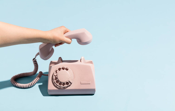 Woman's hand putting a retro telephone reciver down, hanging up. Pastel colors. Blue and pink. - Foto, Imagem