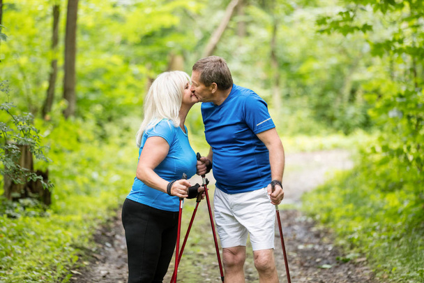 Couple plus âgé embrasser dans les bois tout en trekking. Activités de plein air estivales
. - Photo, image