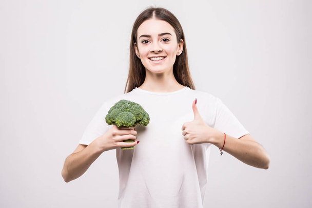 Portret van mooi meisje houdt van broccoli en tonen duimschroef opwaarts gebaar geïsoleerd op witte achtergrond - Foto, afbeelding