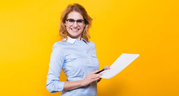 Young blond businesswoman holding documents and pen and looking at camera - Valokuva, kuva