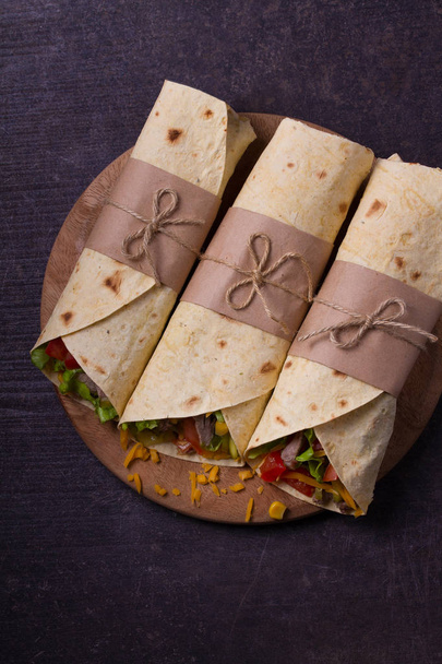 Tortilla, burritos, sandwiches twisted rolls. Wraps with beef, tomatoes, lettuce, cucumbers, cheddar cheese, corn and onion rings. View from above, top, vertical - Fotó, kép