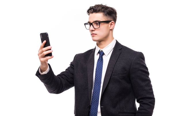 Pohledný mladý muž používající svůj telefon s úsměvem stoje proti bílým pozadím. - Fotografie, Obrázek