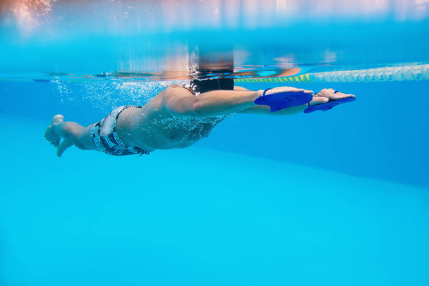 Kavkazská sportovec plavání s lopatkami pro plavání v bazénu pod vodou - Fotografie, Obrázek