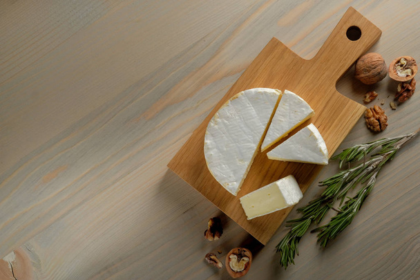Крупный план белого вкусного камамберного сыра с грецкими орехами и розмарином на деревянной доске на фоне стола
  - Фото, изображение