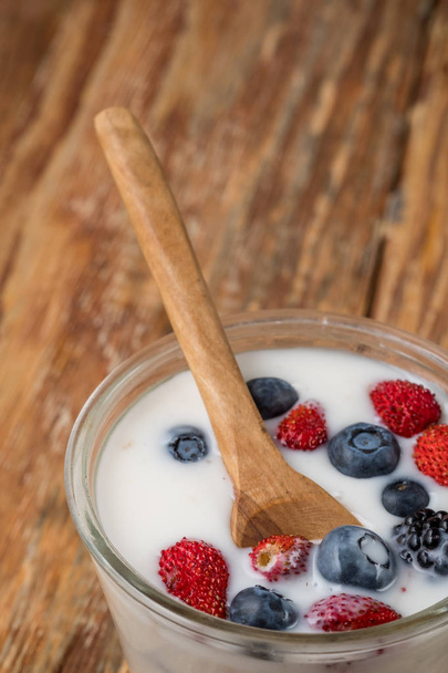 Glass of milkshake with berries and wooden spoon on wooden table, top view - Photo, image