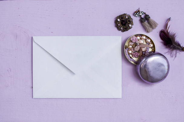 white envelope with jewelery in a round metal box, brooch, earrings flat lay on purple background. - Foto, immagini