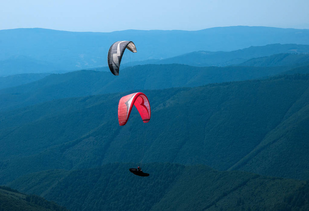 Два парапланериста летят над горной долиной в солнечный летний день
. - Фото, изображение
