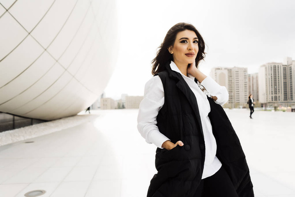 stylish young woman in a black suit posing against the background of the unusual architecture of the city of Baku, smiling - Foto, Bild