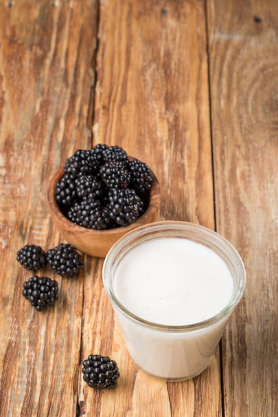 glass of milk and blackberries in wooden bowl on table, top view with copy space - Fotoğraf, Görsel