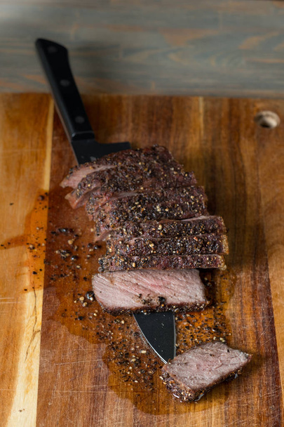 close-up de carne grelhada com especiarias e faca preta em tábua de madeira sobre fundo de mesa
   - Foto, Imagem