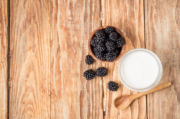 glass of milk, spoon and blackberries in wooden bowl on table, top view with copy space - Foto, imagen