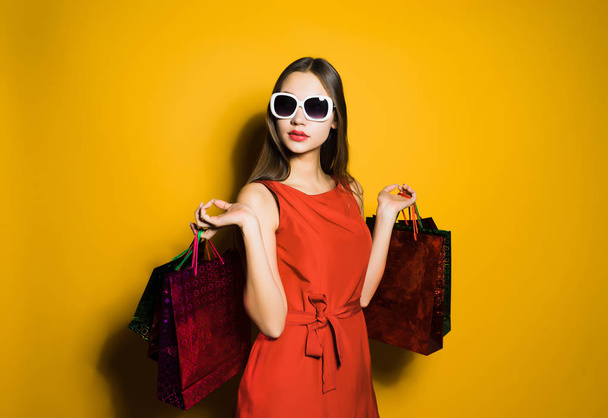 an attractive girl in a red dress and sunglasses bought many presents on a black Friday - Zdjęcie, obraz