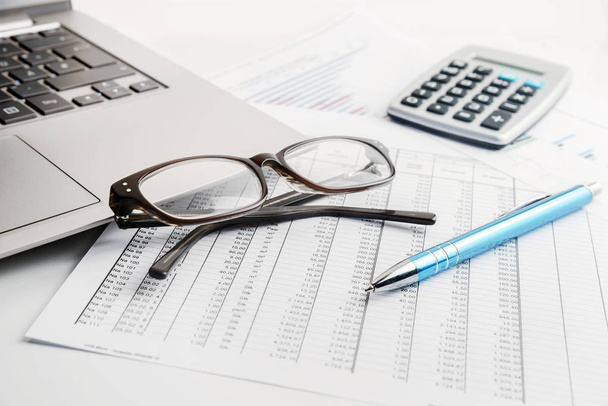 laptop, glasses, pen and calculator lying on a financial report with number tables on the office desk, business concept for finance and taxes, copy space - Photo, image