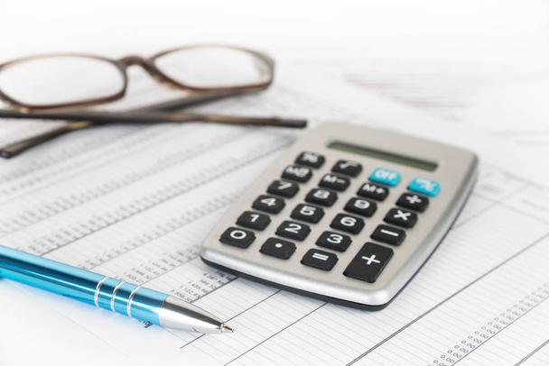 calculator, pen and glasses on a printed financial report with number tables, business concept for finance, economy and taxes - Photo, Image