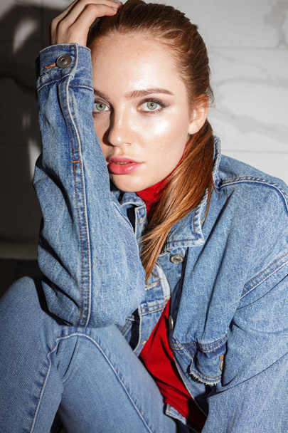 Close up photo of young woman in denim jacket sitting and dreamily looking in camera isolated - Photo, Image