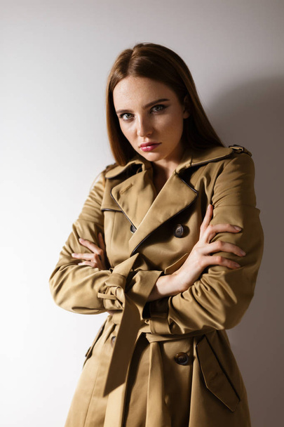 Portrait of beautiful lady in trench coat standing and mysteriously looking in camera isolated - Photo, Image