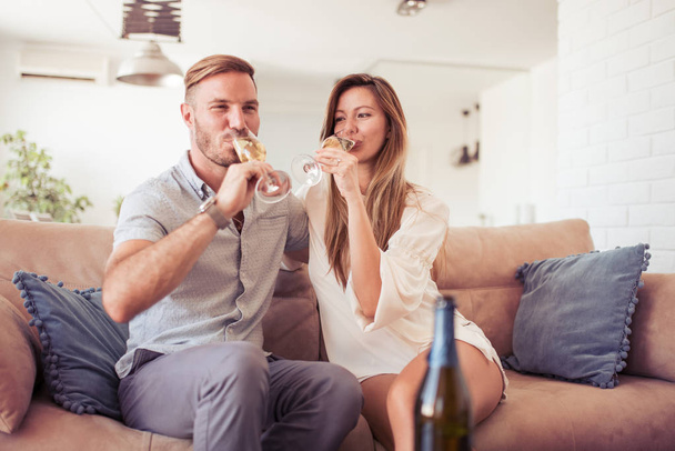 Красивая пара пьет вино, разговаривает и улыбается на диване дома
. - Фото, изображение
