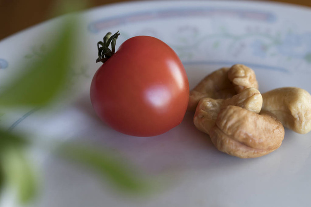 Małe słodkie czerwony pomidor obok niektórych orzechów nerkowca. - Zdjęcie, obraz