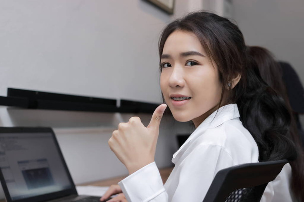 Confident young Asian business woman showing thump up hand sign on office. - Photo, Image