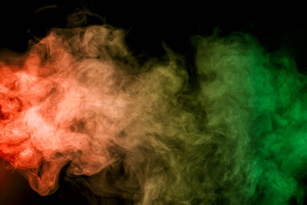 Thick colorful smoke of green, red, yellow on a black isolated background. Background from the smoke of vape - 写真・画像