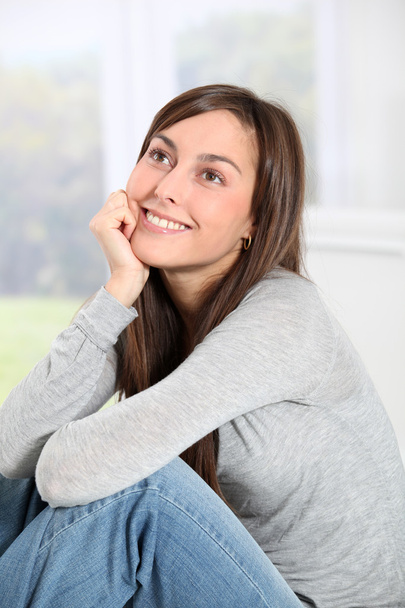 Усміхнена молода жінка вдома сидить на дивані
 - Фото, зображення