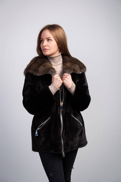 Young dark-haired woman in black fur coat made from natural mink fur posing on white isolated background - Foto, Imagen