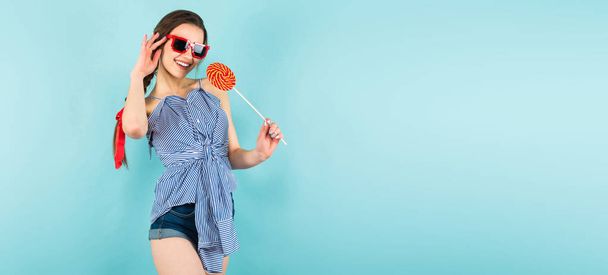 Happy pretty brunette girl holding big spiral lollypop on blue studio background  - Photo, Image