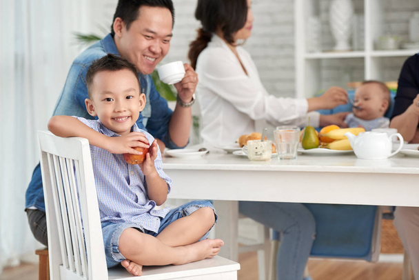 アップルを押しながら家族と朝食用のテーブルに座って、カメラに笑顔幸せなアジア少年の肖像画 - 写真・画像