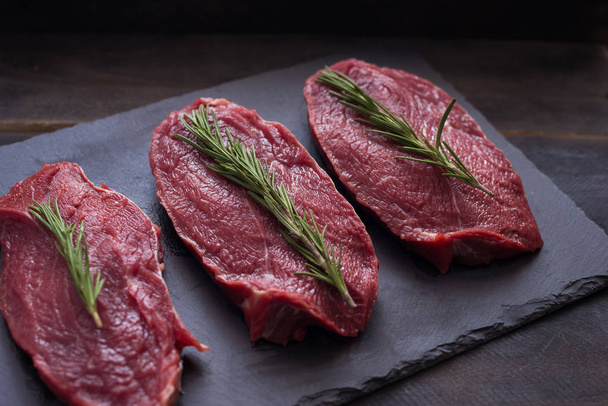Rauw vlees, biefstuk met rozemarijn op zwarte achtergrond. Drie items. Close-up. - Foto, afbeelding