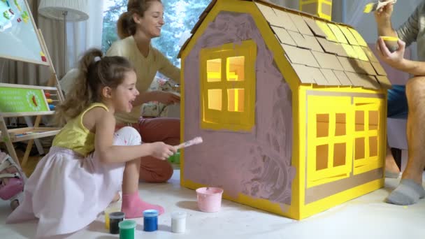 Família jovem com construção infantil e pintura de casa de papelão de brinquedo juntos
. - Filmagem, Vídeo
