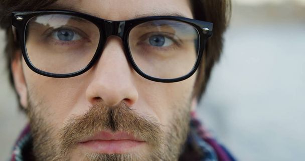 Close up of a shrewd male look. Caucasian man in glasses and plaid scarf. Blurred background. Outdoors. - Photo, Image