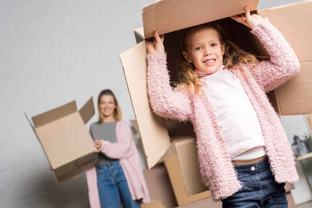 happy mother and daughter holding cardboard boxes while moving home - Photo, Image