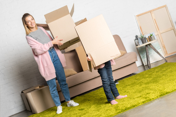 happy mother and little daughter holding cardboard boxes while moving home - Foto, Bild